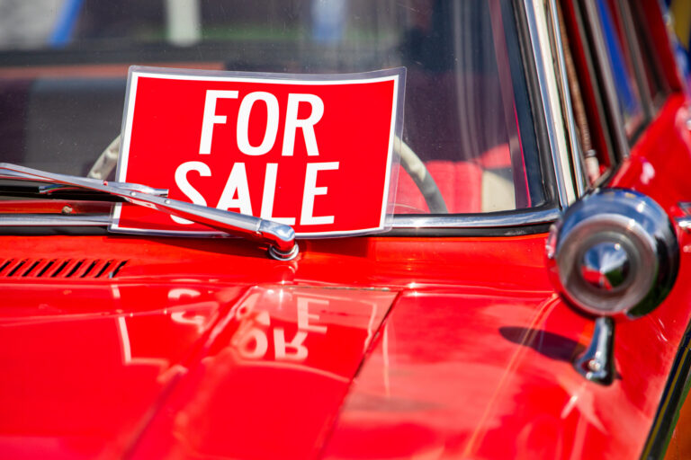 a red for sale sign in the window of a red classic sports car