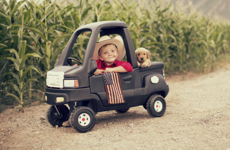 a little boy in his toy car waving an american flag