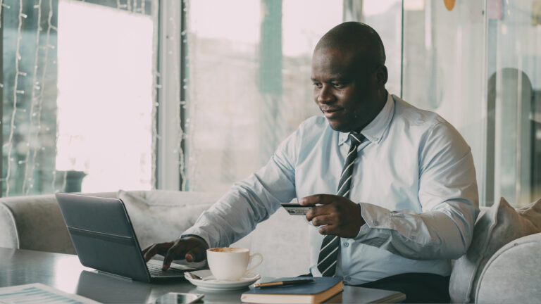 a smiling businessman in a suite paying an online bill with his credit card