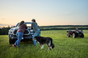 a woman and a man leaning up against their car in a field